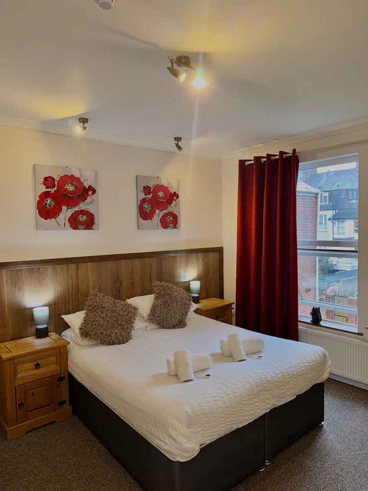 Double room with red poppy canvases, pine bedside cabinets and a large window with red curtains