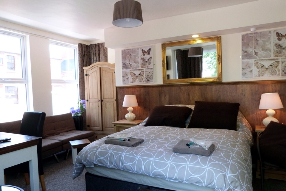 Newly designed double room with oak-panelled headboard wall, sofa, work desk and a gold-framed mirror