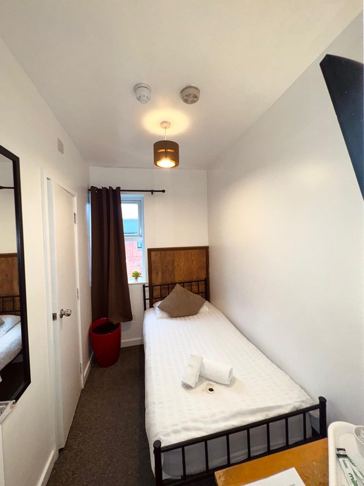Single room with a single bed, a window with brown curtains and a full-length mirror