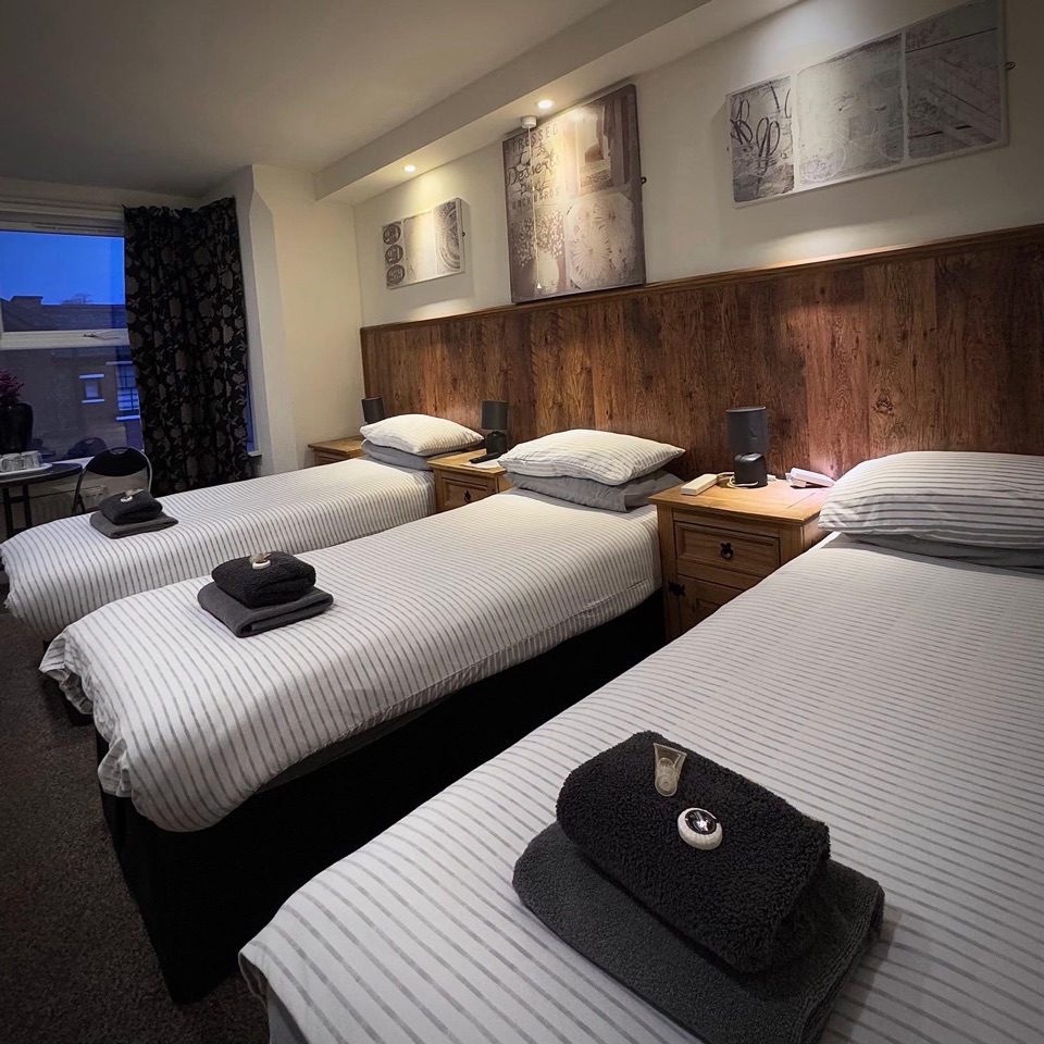 Triple room with three single beds in striped linen along an oak-panelled wall
