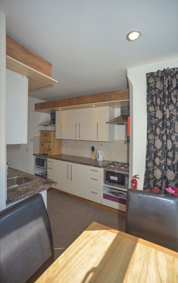 Room with a full kitchen: hob, oven, microwave and worktop beside a dining table